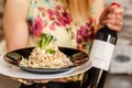 Close up on midsection of unknown caucasian woman holding a plate of cooked carbonara pasta spaghetti in a plate with bottle of