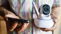 Close up on midsection of unknown man holding home security surveillance camera and mobile phone trying to install an app front Royalty Free Stock Photo