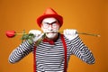 Close up mime with white face in red hat and striped T-shirt holding rose in his mouth on blank orange background Royalty Free Stock Photo