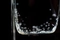 Close up of mineral water bubbles in the glass. Fresh sparkling drink with oxygen balls on dark background