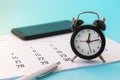 Close up of mini alarm clock, calendar and white pen and smartphone on blue background. Business meeting planning, deadline Royalty Free Stock Photo