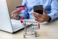 Close up mini cart, Asian businessman holding credit card using laptop and smart phone for online shopping while making orders. Royalty Free Stock Photo