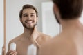 Close up mirror reflection overjoyed young man applying aftershave lotion Royalty Free Stock Photo