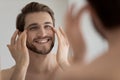 Close up mirror reflection smiling man touching skin under eyes