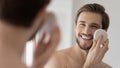 Close up mirror reflection smiling man using facial cleansing sponge Royalty Free Stock Photo