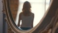 Close-up of mirror reflection of young blond woman in white t-shirt and blue jeans walking near a window in her