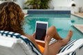 Woman using digital tablet while relaxing on a sun lounger near swimming pool at the backyard of hom Royalty Free Stock Photo