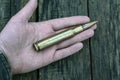 Close up of 50 mm caliber bullet in mans hand on wooden background