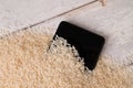 A close-up of a mobile phone placed to dry in a pile of rice after the phone fell into water. Light wooden table background. Top