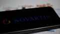 Close up of mobile phone screen with logo lettering of Novartis pharmaceutical company, blurred pills and lab sheet background Royalty Free Stock Photo