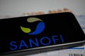 Close up of mobile phone screen with logo lettering of Sanofi pharmaceutical company, blurred pills and lab sheet background