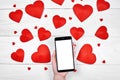 Close up of mobile smart phone with blank white screen for app presentation  in female hand and red paper hearts on wood Royalty Free Stock Photo