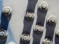 A close-up of a mock of large hex nuts with a washer secured by threaded studs to iron surface. Long, thick shadows