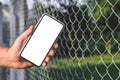 Close-up, Mockup of a smartphone in the hand of a man. Against the background of a steel wire fence and nature Royalty Free Stock Photo