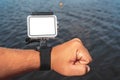 Close-up, mockup of a waterproof action camera with mounts on a man& x27;s hand. Against the backdrop of the blue water of the sea