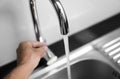 Male hand and close up on modern kitchen metal faucet and metal kitchen sink with a running water. Royalty Free Stock Photo