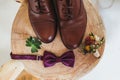 Close up of modern man accessories. purple bow-tie, leather shoes, belt and flower boutonniere on wood chair rustic.