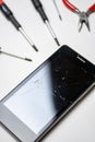 Smartphone with broken and cracked screen with screwdrivers and pliers on white background. Vertical Royalty Free Stock Photo