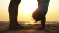 Silhouette of mother with daughter doing gymnastic on the beach at sunset