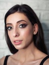 Close up mood portrait of young beautiful woman with gorgeous long brunette hair showing trendy facial makeup indoors