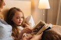 Close-up of mother and happy daughter reading together children book before going to sleep while lying in bed Royalty Free Stock Photo