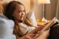 Close-up of mother and smiling adorable daughter reading together children book before going to sleep while lying in bed Royalty Free Stock Photo