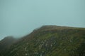 Close up of a mountain with green grass all over it during a foggy day with mist all over it with copy space Royalty Free Stock Photo