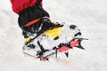 Close up of Ã¢â¬Å½mountaineering crampons with visible sharp teeth on a foot with gaiters, on snow. Winter hiking, equipment, gear