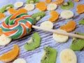 Close-up of multi-colored candy on a background of slices of kiwi, tangerine / orange, bananas on an abstract wooden surface Royalty Free Stock Photo