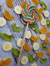 Close-up of multi-colored candy on a background of slices of kiwi, tangerine / orange, bananas on an abstract wooden surface Royalty Free Stock Photo