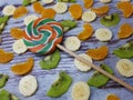 Close-up of multi-colored candy on a background of slices of kiwi, tangerine / orange, bananas on an abstract wooden surface Royalty Free Stock Photo