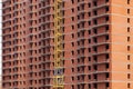 Close-up on a multi-storey residential building under construction from red brick with a part of a yellow crane. The walls of the Royalty Free Stock Photo