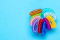 Close-up of multicolored elastic spiral scrunchies or hair bands for women hairstyling over blue background. Hair care tools from