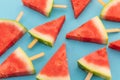 Close up of multiple watermelon triangles on wooden sticks on blue background