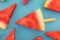 Close up of multiple watermelon triangles on wooden sticks on blue background