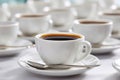 Close-up of multiple white coffee cups filled with dark brewed coffee arranged on a white tablecloth, emphasizing the front cup Royalty Free Stock Photo
