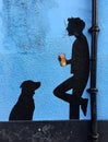 Close up mural of man drinking beer with his dog in black on blue wall
