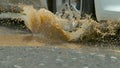 CLOSE UP: Murky water splashes across asphalt road as car drives into puddle. Royalty Free Stock Photo