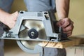 Close-up of muscular carpenter hands using new shiny modern powerful circular sharp electrical saw for cutting hard wooden board. Royalty Free Stock Photo