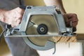 Close-up of muscular carpenter hands using new shiny modern powerful circular sharp electrical saw for cutting hard wooden board. Royalty Free Stock Photo