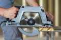 Close-up of muscular carpenter hands using new shiny modern powerful circular sharp electrical saw for cutting hard wooden board. Royalty Free Stock Photo