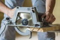 Close-up of muscular carpenter hands using new shiny modern powerful circular sharp electrical saw for cutting hard wooden board. Royalty Free Stock Photo