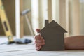 Close-up of muscular male hand holding small model house on blurred background of building tools in room under construction. Inves Royalty Free Stock Photo