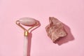 Close up of natural raw pink rose quartz rough stone and facial massage roller isolated over pink background Royalty Free Stock Photo