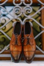 A close-up of new brown mens shoes against the metal bars of the window.