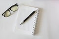 Close up of notebook with ink-pen and eyeglasses put on white table with blur focus of books as a background. Royalty Free Stock Photo