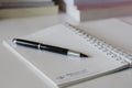 Close up of notebook with ink-pen and eyeglasses put on white table with blur focus of books as a background. Royalty Free Stock Photo