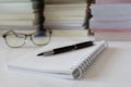 Close up of notebook with ink-pen and eyeglasses put on white table with blur focus of books as a background. Royalty Free Stock Photo