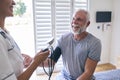 Close Up Of Nurse Wearing Uniform Taking Blood Pressure Of Senior Man In Private Hospital Room