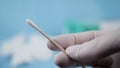 Close up of nurse with white gloves holding swab for coronavirus testing. Medical environment.